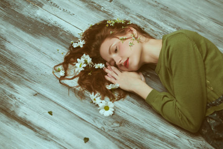 Women's beauty and fashion. A beautiful tender girl with wavy red hair poses on the floor in an olive green dress with white flowers in her hair. Copy space. Spring and summer mood.の写真素材