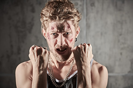 A portrait of a brutal man with scratches and wounds on his face, who stands in front of concrete...