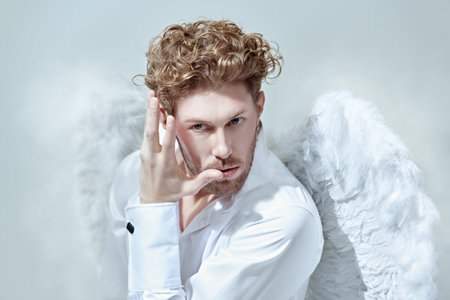 Courageous handsome male Cupid angel in white clothes and with white wings. Skylight in the background. God of love Cupid. Valentine's Day.の写真素材