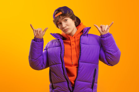 Portrait of a trendy teenage boy in bright orange hoodie, purple jacket and baseball cap. Yellow...