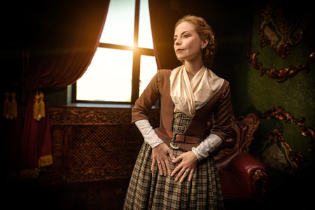 A beautiful aristocratic girl in an 18th century Scottish dress standing peacefully in a room with...