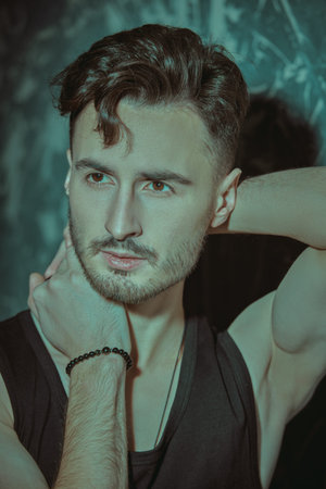 Portrait of a handsome young brunet man of athletic build posing in a black tank top against a...