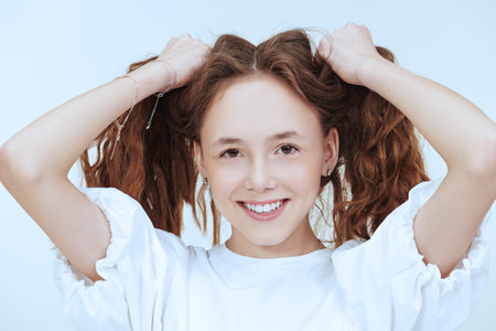 Happy children concept. Portrait of a beautiful teenage girl with long wavy hair smiling at camera....