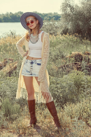 Fashion shot of a beautiful fair-haired girl in boho style clothes and jewelry posing outdoors on a sunny summer day. Summer bohemian and hippie style. Fashion and beauty.の写真素材