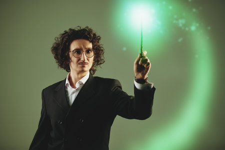 Inspired male magician waves his stick. The miracle and focus. Inspiration. Studio portrait on a gray background.の写真素材