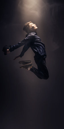 Studio full-legth portrait of a jumping teenage boy in stylish youth clothes on a dark grey background. Casual style for teenagers. Psychology, emotions.の写真素材