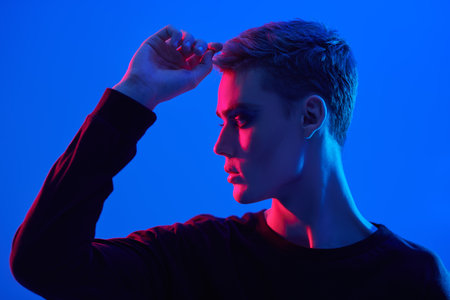 Art shot of a sensual handsome young man posing at studio on a blue background in mixed colored neon light. Male beauty. Art Fashion concept.の写真素材