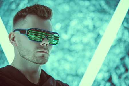 Portrait of cyberpunk man of the future in green virtual reality glasses and black mantle standing among neon lamps. World of the future. Game, virtual reality. Future technologies.の写真素材
