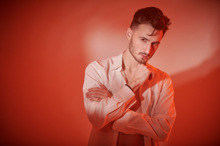 Classic fashion and male beauty. Portrait of a handsome man posing in a classic white shirt in the red studio light. Copy space.の写真素材