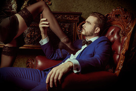 A shot of a man flirting with his girlfriend passionately embracing his girlfriend's leg in a luxury apartments. Love and passion. Evening Fashion.の写真素材