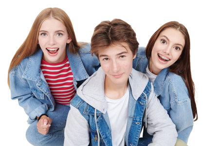 Fashion shot of two pretty teen girls and a handsome teen boy in trendy denim clothes posing on a white studio background. Denim fashion, teenage style. Education.の写真素材