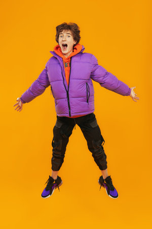 Casual fashion for teens. Lifestyle of the modern teenager. A teenager boy in fashionable bright clothes flies through the air, being very surprised. Studio yellow background with copyspace.の写真素材