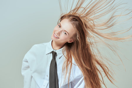 Beauty and Fashion. Portrait of a beautiful fashion model girl posing in dance at the studio in classic style clothes - a white blouse, a black tie. White background with copy space.の写真素材