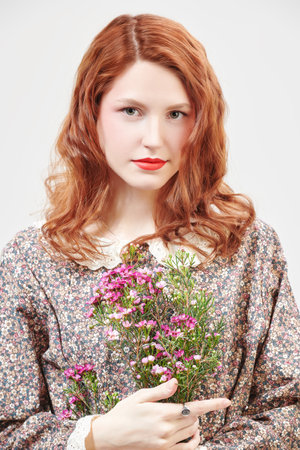 Portrait of a beautiful  girl with delicate fresh make-up posing against a white wall in a floral dress with flowers. Spring and summer fashion. Romantic feminine style.の写真素材