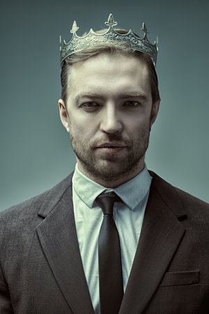 The concept of success. Portrait of a handsome well-groomed mature man dressed in a business suit and with a crown on his head, who looks calmly and confidently. Business and successful lifestyle.の写真素材