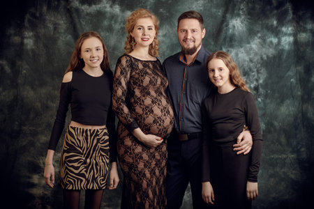 Beautiful happy mother and father with their beloved daughters posing together on a grunge studio...
