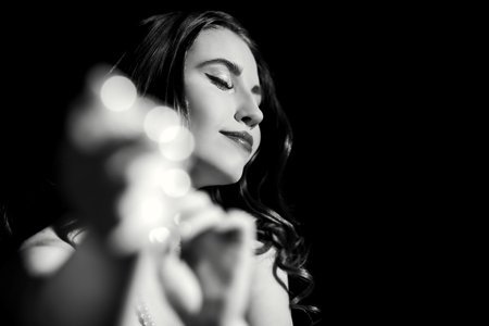 Black and white portrait of a beautiful young woman with long wavy hair and elegant evening make-up, who closed her eyes and smiles. Black background. Retro style. The actress is playing a role.の写真素材