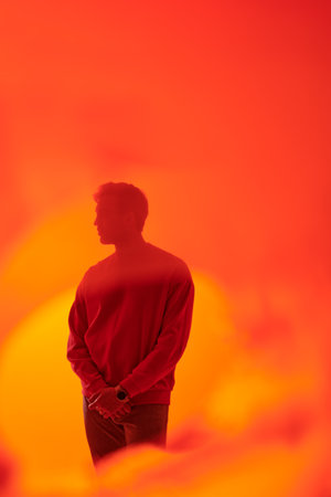 An art shot of a handsome mature man standing sideways and looking thoughtfully ahead. Studio portrait with haze in orange light. Psychology, emotions.の写真素材