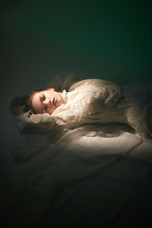 Art portrait of a beautiful tender girl with long hair, who lies on the floor in a white lace dress. Beauty and Fantasy. Copy space.の写真素材