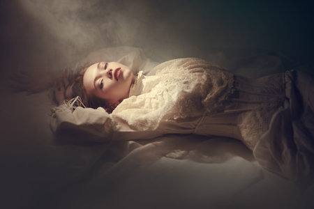 Art portrait of a beautiful tender girl with long hair, who lies on the floor in a white lace dress shrouded in haze. Beauty and Fantasy.の写真素材