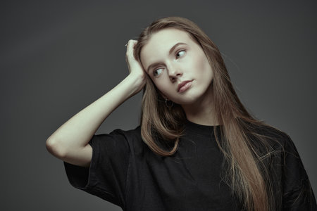 Psychological art portrait. A beautiful tender girl with long red hair is sad about something. Dark gray studio background.の写真素材