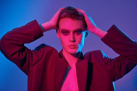 Art portrait of a sensual handsome young man posing at studio on a blue background in mixed colored neon light. Male beauty. Art Fashion concept.の写真素材