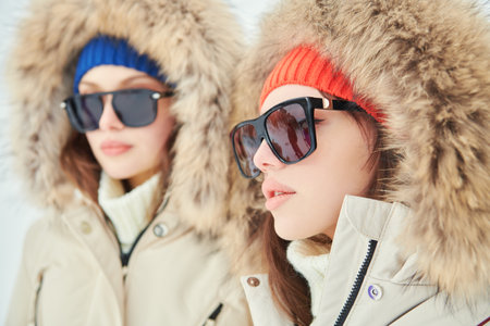 Portrait of two fashion model girls posing in white downy overalls against outdoors. Alpine skiing, active winter recreation. Winter fashion.の写真素材
