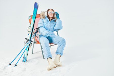A happy girl in a blue ski suit is resting in a ski resort. Winter fashion, clothes and accessories. Winter active rest. Copy space.の写真素材