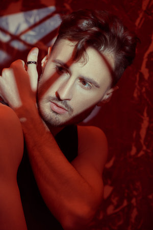 Art portrait of a masculine handsome brunette man standing in a dark room with shadows. Mixed lighting, light and shadows.の写真素材