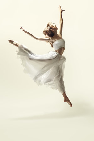 A young graceful ballerina in a delicate white dress dances with expression. Modern ballet dancer. Full-length studio portrait.の写真素材