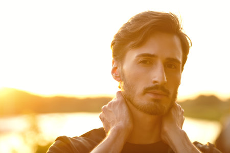 Close up portrait of a young man standing thoughtfully outdoors on the background of a river at sunset. People and emotions.の写真素材