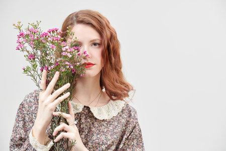 Portrait of a beautiful  girl with delicate fresh make-up posing against a white wall in a floral dress with flowers. Spring and summer fashion. Romantic feminine style. Copy space.の写真素材