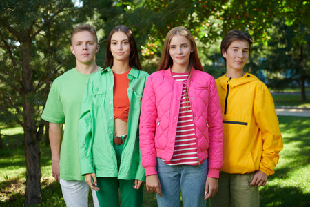 Portrait of four friends teenagers in colourful summer clothes walking together in a sunny park. Bright summer fashion. Youth lifestyle.の写真素材