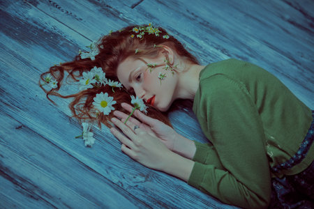 A beautiful tender girl with wavy hair lying on a wooden floor with white flowers in her hair. Natural cosmetics. Women's beauty and fashion. Spring and summer mood. Copy space.の写真素材