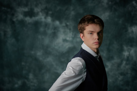 Men's fashion, Classic style. A portrait of a well-groomed young man wearing an elegant vest, trousers and a white shirt with cufflinks on a vintage background with copy space.の写真素材