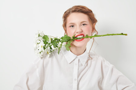 Beauty portrait of a pretty girl with delicate makeup and curly red hair posing with white chrysanthemums on a white background. Cosmetics and perfumery. Women's beauty and flowers.の写真素材