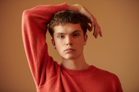 Portrait of a modern young man looking calmly and thoughtfully. Studio brown background. Bright colours.の写真素材