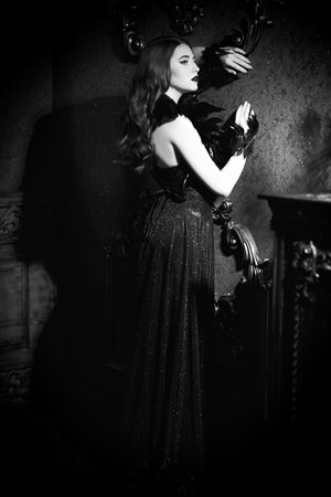 Black-and-white shot. Beautiful brunette woman with wavy hair posing in an elegant evening dress in a luxury vintage interior. Elegant retro style.の写真素材