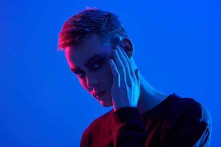 Art shot of a sensual handsome young man posing at studio on a blue background in mixed colored neon light. Male beauty. Art Fashion concept.の写真素材