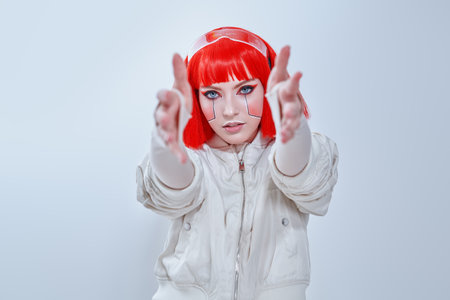 Portrait of an attractive sci-fi cyborg girl with bright red makeup and stylish red hair. Cyberpunk concept. Make-up and hairstyle. White background with copy space.の写真素材