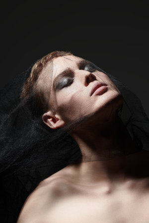 Portrait of a young man fashion model covering his head with black mesh fabric. Black background. Male beauty and fashion. Art and Fashion.の写真素材