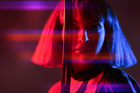An attractive cyberpunk girl stands on alert with a sword against a red background. Sci-fi cyborg soldier girl. Game, virtual reality.の写真素材
