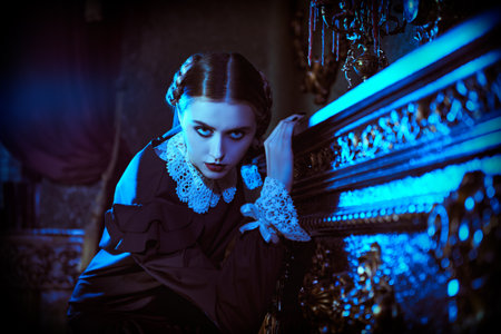 Gothic novel. A serious brunette girl in a strict black dress with a white collar stands by the fireplace in a gloomy mansion at night. The Addams Family.の写真素材