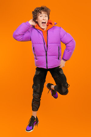 A teenager boy in fashionable bright clothes flies through the air, being very surprised. Studio yellow background. Casual fashion for teens. Lifestyle of the modern teenager.の写真素材
