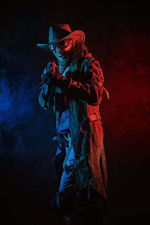 Post apocalyptic cowboy. A furious man in a leather coat,  cowboy hat and goggles shoots with a...