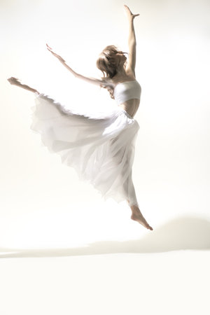 Choreography. A young graceful ballerina in a delicate white dress dances with expression. Full-length studio portrait. Modern ballet dancer.の写真素材