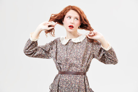 Portrait of a beautiful ginger girl with delicate fresh make-up posing against a white wall in a floral dress. Spring and summer fashion. Romantic feminine style.の写真素材
