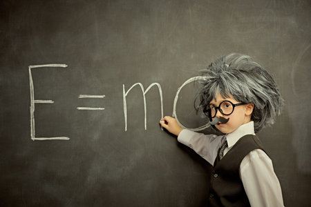 A funny cute child in glasses, with a mustache and in a wig, like a little Einstein, writing a...