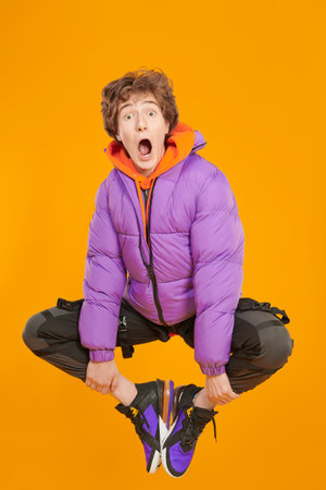 Lifestyle of the modern teenager. A teenager boy in fashionable bright clothes flies through the air, being very surprised. Studio yellow background. Casual fashion for teens.の写真素材