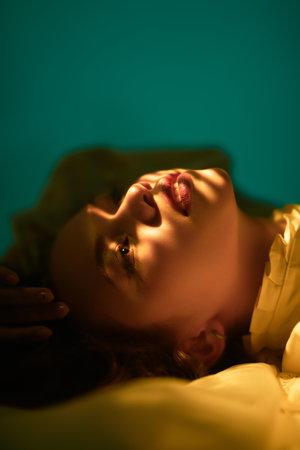 Art, Beauty and Fantasy. Portrait of a beautiful tender girl with long hair, who lies on the floor in a white lace dress and gazes upward. Light and shadows play on her face.の写真素材